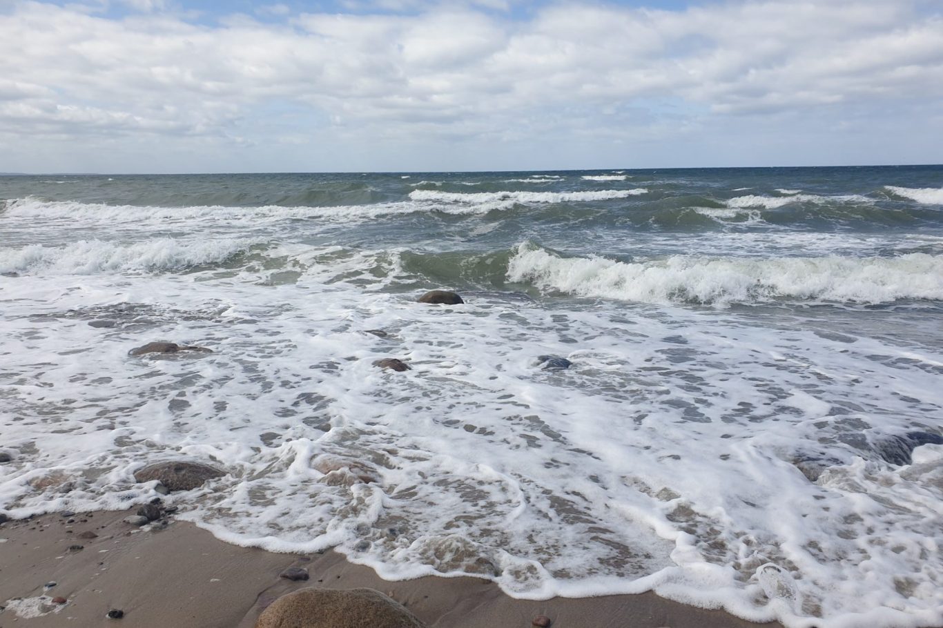 Wellen brechen an einem sandigen Strand unter einem bewölkten Himmel.